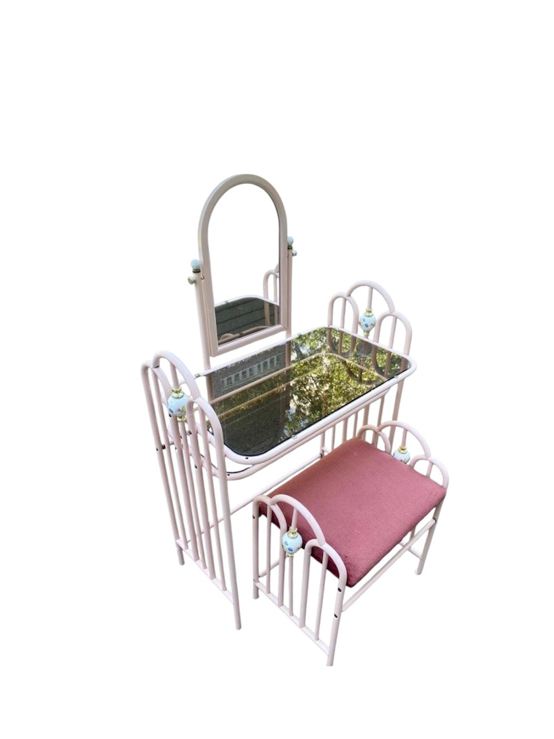 A vanity furniture set featuring a vanity table with an arched mirror, a small bed with a pink cushion, and a matching chair, all in a light pink metal frame.