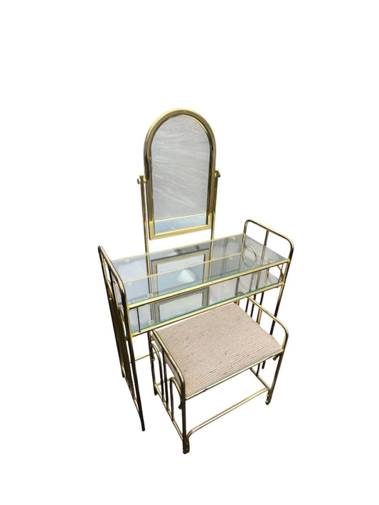 A mid-century modern vanity table set with a gold metal frame, clear glass top, arched mirror, and a matching marble-patterned stool, isolated on a white background.