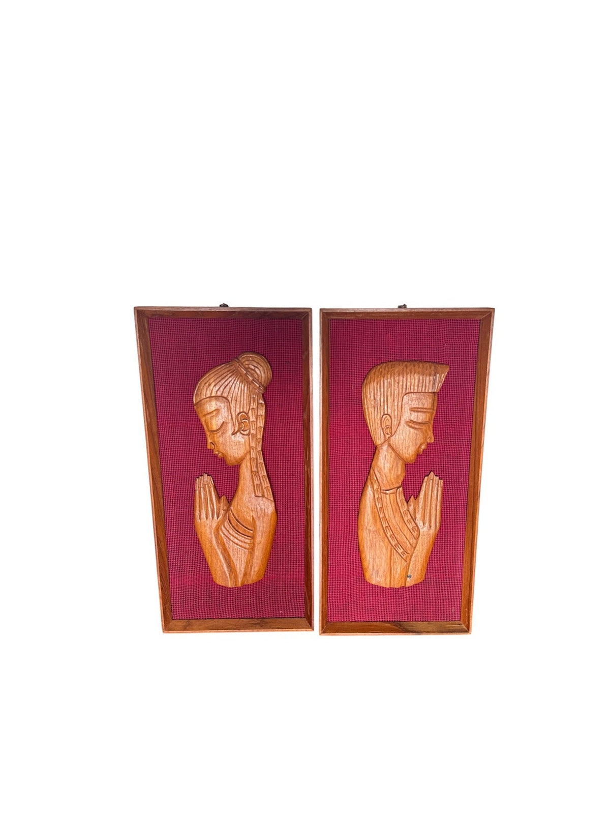 A pair of rectangular framed wall art pieces featuring carved wooden figures in profile with hands together in a prayer pose, set against a deep magenta background.