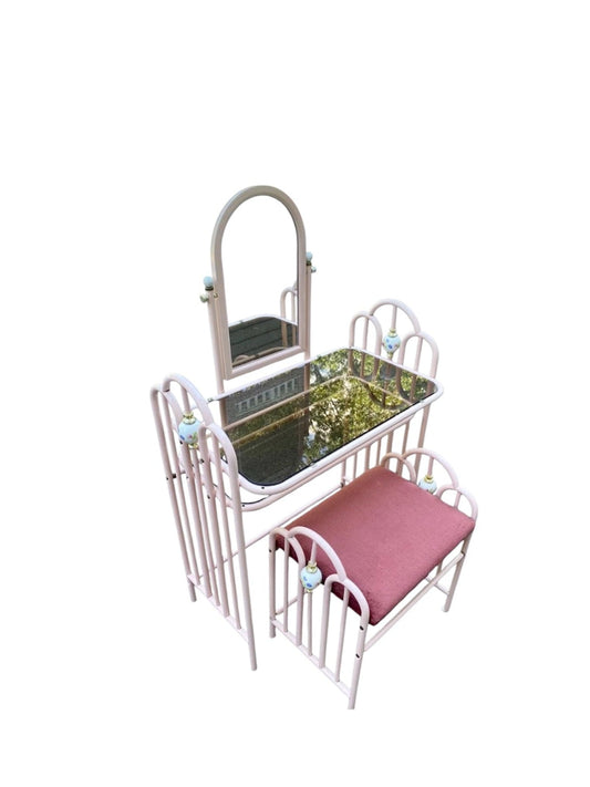 A vanity furniture set featuring a vanity table with an arched mirror, a small bed with a pink cushion, and a matching chair, all in a light pink metal frame.